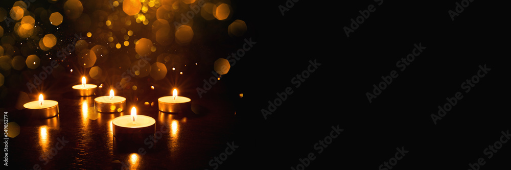 Several burning candles with festive bokeh on a black background. Banner with copy space. Several burning candles with festive bokeh on a black background. Banner with copy space.