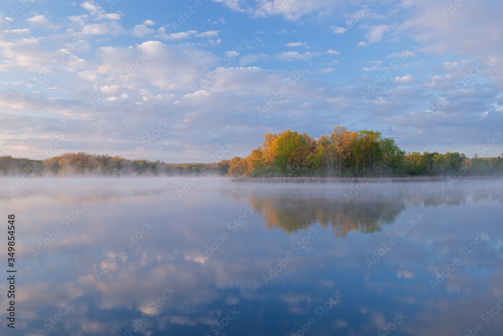 Landscape at sunrise of the foggy, spring shoreline of Whitford Lake with reflections in calm water, Fort Custer State Park, Michigan, USA