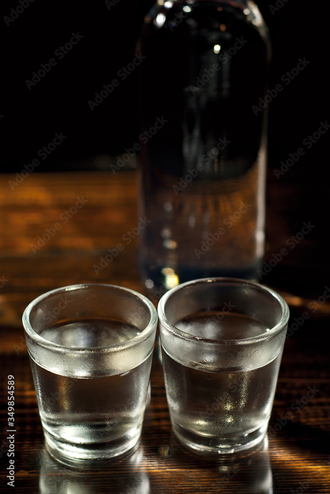 Frozen glasses with alcohol near the bottle. Drinks on a dark brown table. Transparent utensils on a black background. Old shabby boards under glass. Frozen glasses with alcohol near the bottle. Drinks on a dark brown table. Transparent utensils on a black background. Old shabby boards under glass.