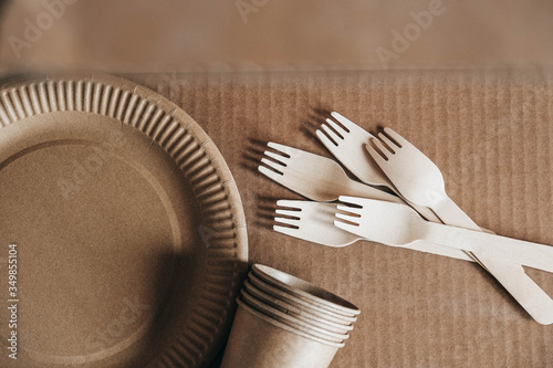 Wooden forks and paper cups with plates on kraft paper background. Eco friendly disposable tableware. Also used in fast food, restaurants, takeaways, picnics. Top view. Copy, empty space for text