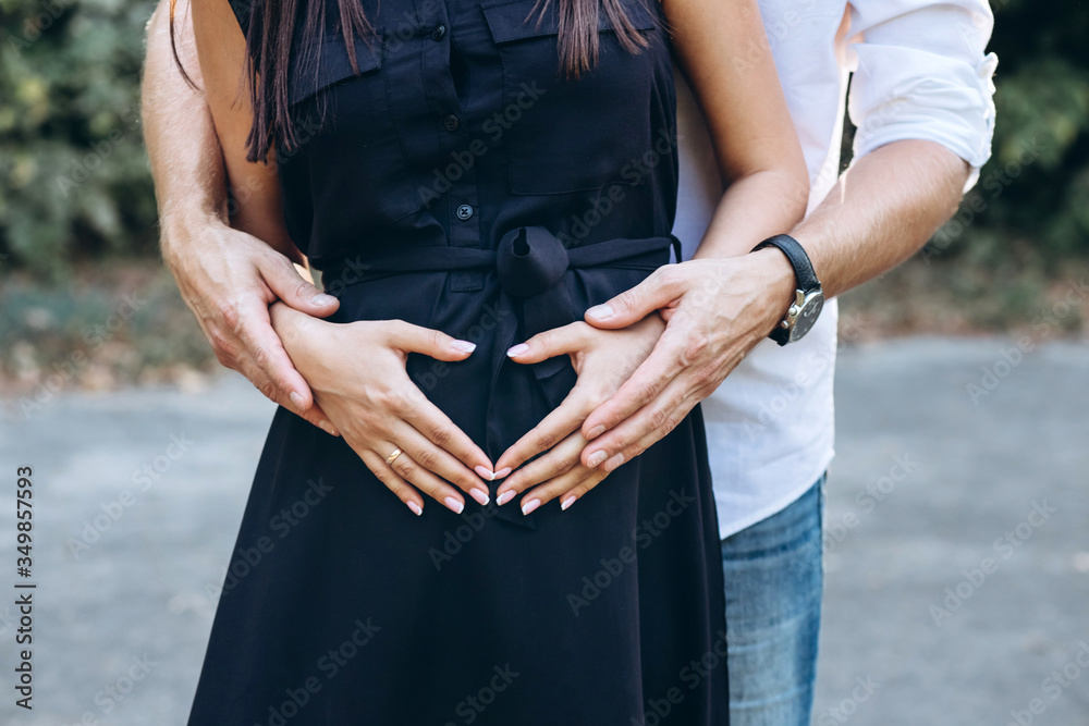 Future parents. A young pregnant woman walks in nature. Hands on the belly close-up. Waiting for a miracle. A man and a woman hold their hands in the shape of a heart.
