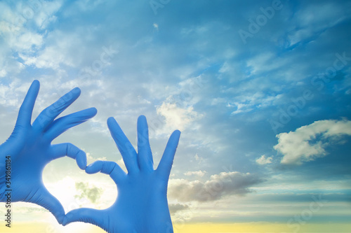 Medicine concept. Doctor hands in blue medical surgical gloves making heart on sky clouds background