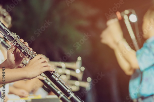 Male student with friends blow the clarinet with the band for performance on stage at night.
