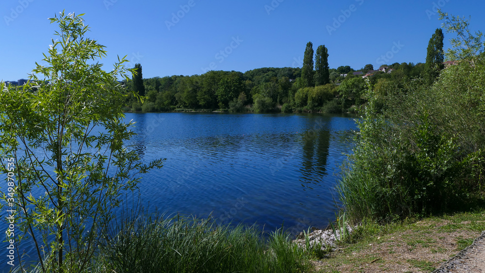 Country landscape with a lake. Sunny blue sky without clouds. A place of relaxation at the water's edge. Stone wall in the foreground.
