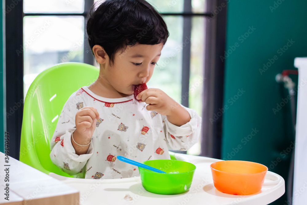 Photo of adorable young happy child toddler boy eating strawberry smiling close up looking at camera. Photo of adorable young happy child toddler boy eating strawberry smiling close up looking at camera.