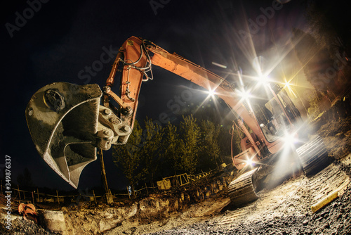 Orange excavator digger working at night on the street