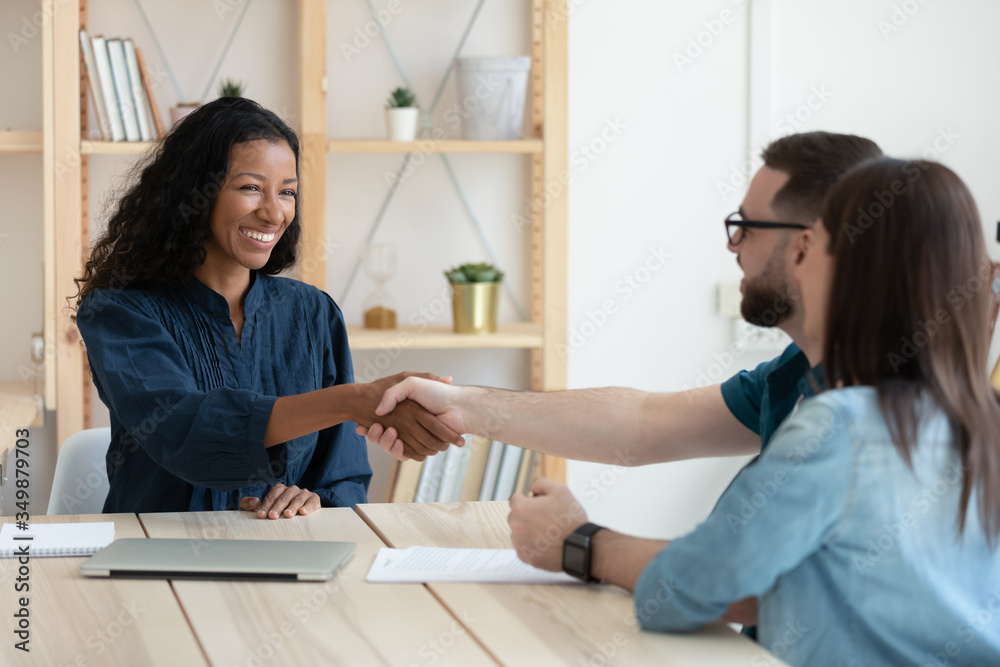 Real estate agent shaking hands with happy young couple in office at meeting. Smiling millennial family clients take congratulation on buying house rent and mortgage by financial advisor. Real estate agent shaking hands with happy young couple in office at meeting. Smiling millennial family clients take congratulation on buying house rent and mortgage by financial advisor.