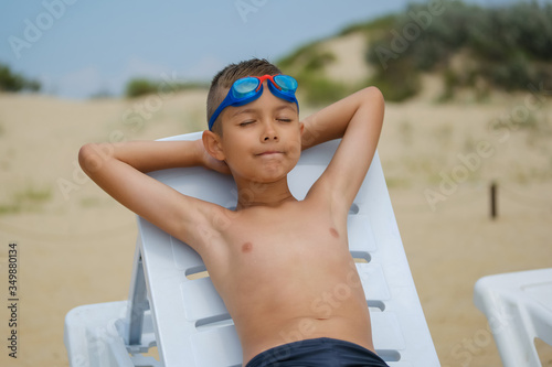 Young guy in swimming glasses is sunbathing on a sunbed on the sea beach.