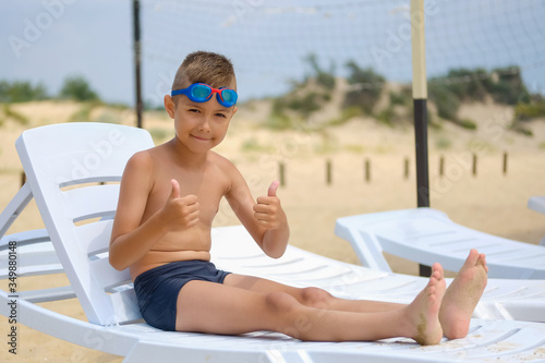 Young guy in swimming glasses is sunbathing on a sunbed on the sea beach.