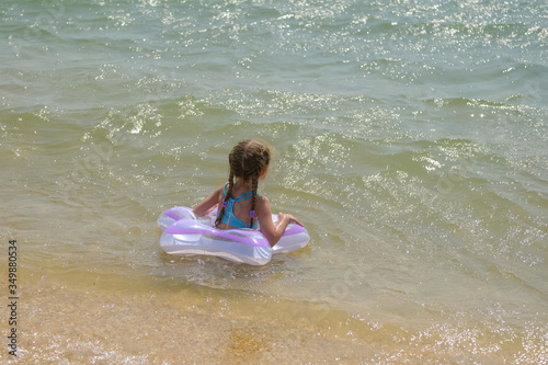 Little girl in an inflatable circle on the beach. A child bathes in the sea.