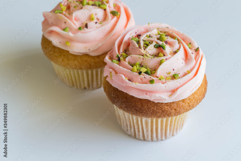 Pink cupcakes on white background - frosted cup cakes decorated with green pistachio sprinkles - with selective focus Pink cupcakes on white background - frosted cup cakes decorated with green pistachio sprinkles - with selective focus