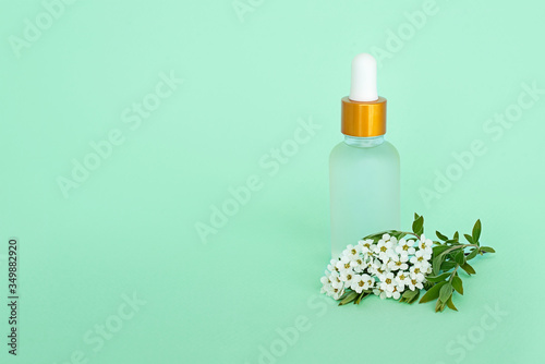 Glass cosmetik bottle with oil. container for a product for women with small white flowers on a turquoise background. Cosmetic jar. Place for text photo