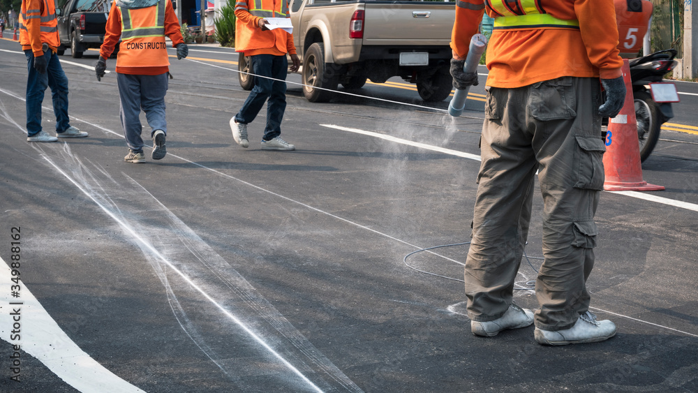 Naklejka premium Low section of road workers group are working to marking line for painting traffic color lines on asphalt road while still driving around in the city, focus at man on foreground