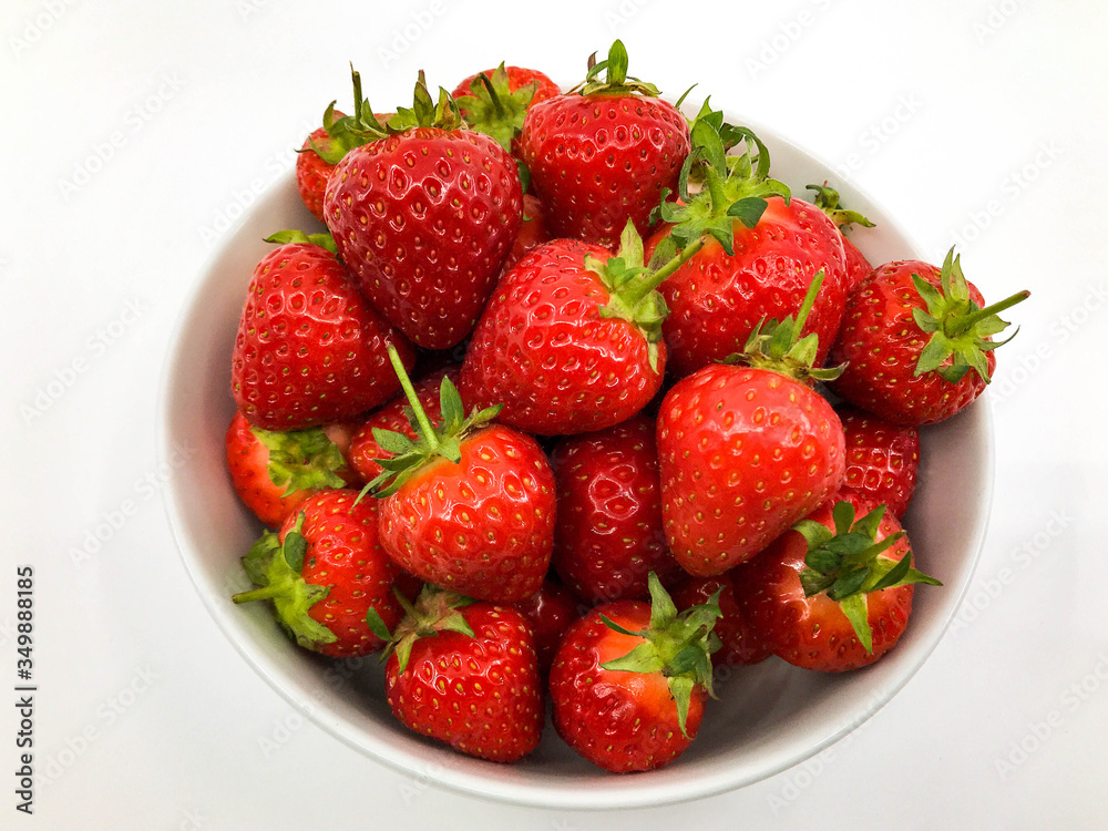 Plump ripe fresh strawberries in a white bowl on a plain white background. Plump ripe fresh strawberries in a white bowl on a plain white background.