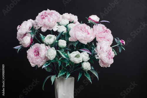 Decoration artificial peonies and white roses in vase on wood chair on black background