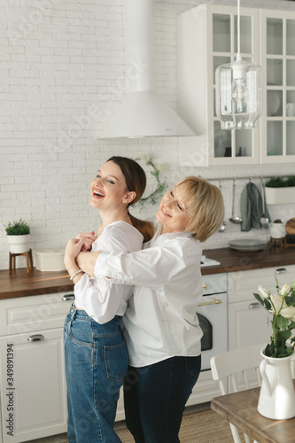 Happy loving older mature mother and grown daughter laughing embracing, caring smiling young woman embracing happy senior middle aged mom having fun at home spending time together
