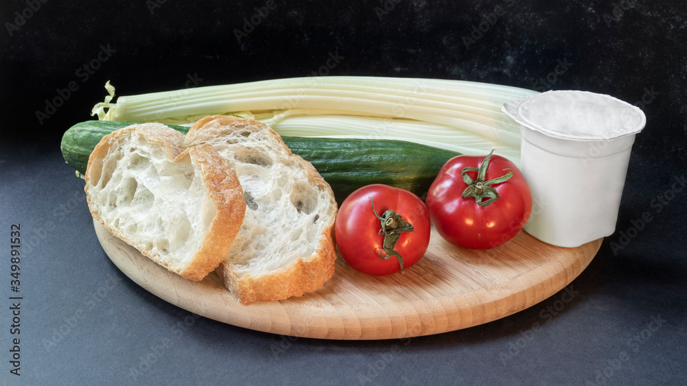 Two slices of white beautiful airy white bread, yogurt, fresh vegetables - cucumbers, tomatoes and celery, all on a round wooden cutting board on a black background close-up.
