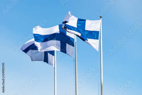 Three finnish national flags on the wind against the blue sky