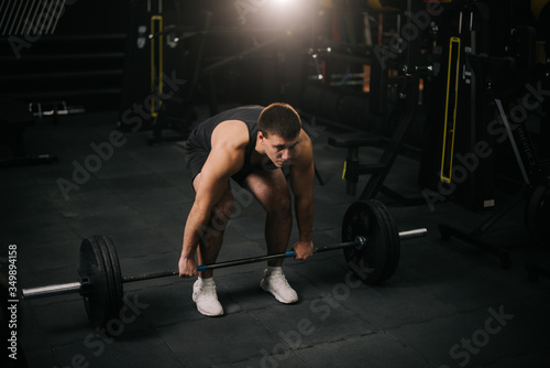 Muscular strong man with perfect beautiful body wearing sportswear lifting heavy barbell from floor during sport workout training in modern dark gym. Concept of healthy lifestyle.
