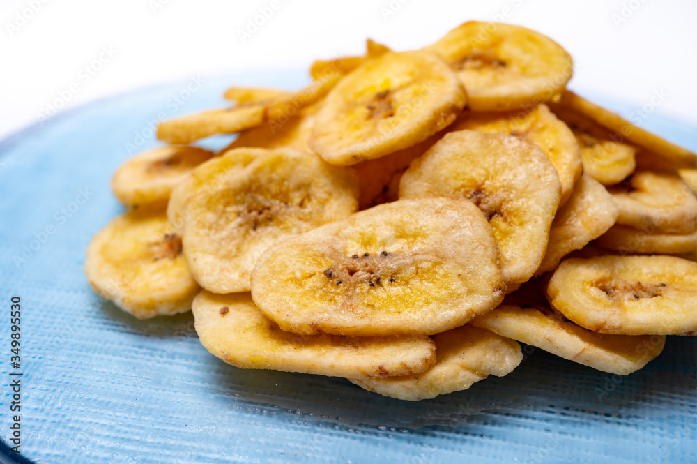 Healthy snack, crispy dehydrated unsugared banana chips on recycled glass plate on white background