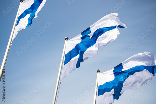 Three finnish national flags on the wind against the blue sky