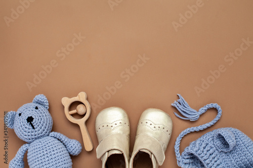 Flat lay composition with baby accessories set: crib shoes, teddy bear toy, knitted hat, wooden rattle and copy space. photo