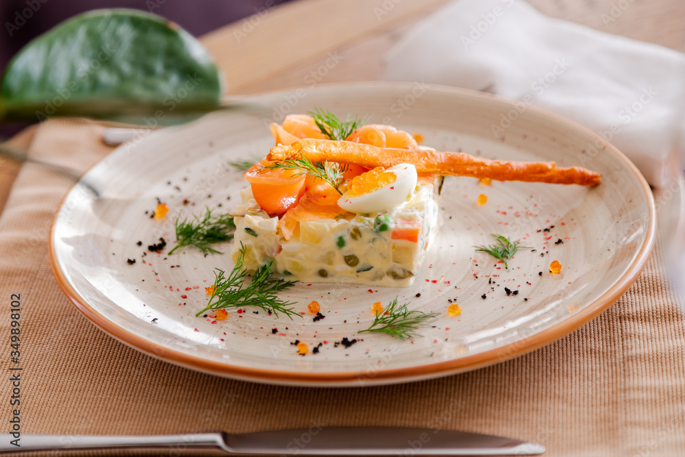 Traditional Russian salad Olivier. Salad is decorated with salmon and quail egg. Against the background of a wooden served table Traditional Russian salad Olivier. Salad is decorated with salmon and quail egg. Against the background of a wooden served table