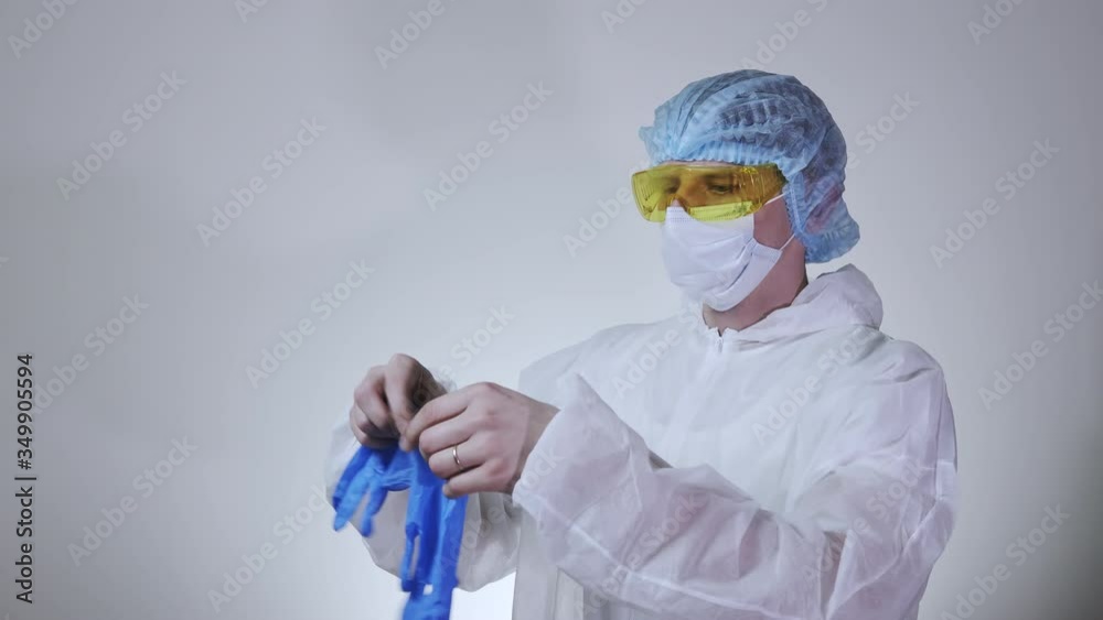 Close-up of young male doctor in the protective suit putting on surgical gloves. Concept of health care, hospitals or clinic and coronavirus pandemic Close-up of young male doctor in the protective suit putting on surgical gloves. Concept of health care, hospitals or clinic and coronavirus pandemic
