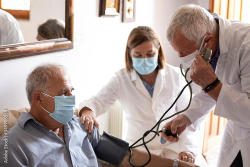 Foto Anziano con mascherina viene visitato da un medico a casa che gli prende la pres