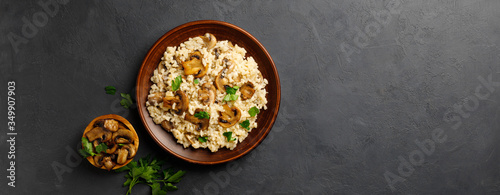 A dish of Italian cuisine - risotto from rice and mushrooms in a brown plate on a black slate background. Top view. Flat lay. Copy space. photo