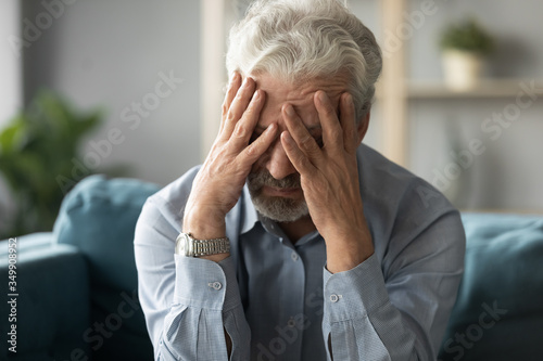 Schilderij op canvas Frustrated unhealthy senior mature man touching head, having painful feelings sitting alone at home