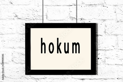 Black frame hanging on white brick wall with inscription hokum
