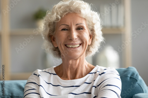 Close up head shot portrait middle aged senior happy woman relaxing on comfortable sofa, enjoying weekend lazy time at home. Pleasant beautiful healthy older mature grandmother looking at camera.