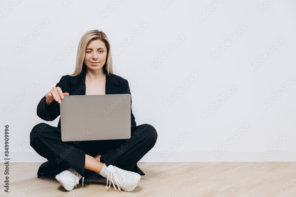 A beautiful young woman is sitting on the floor with a notebook pc on her lap, against a light background A beautiful young woman is sitting on the floor with a notebook pc on her lap, against a light background