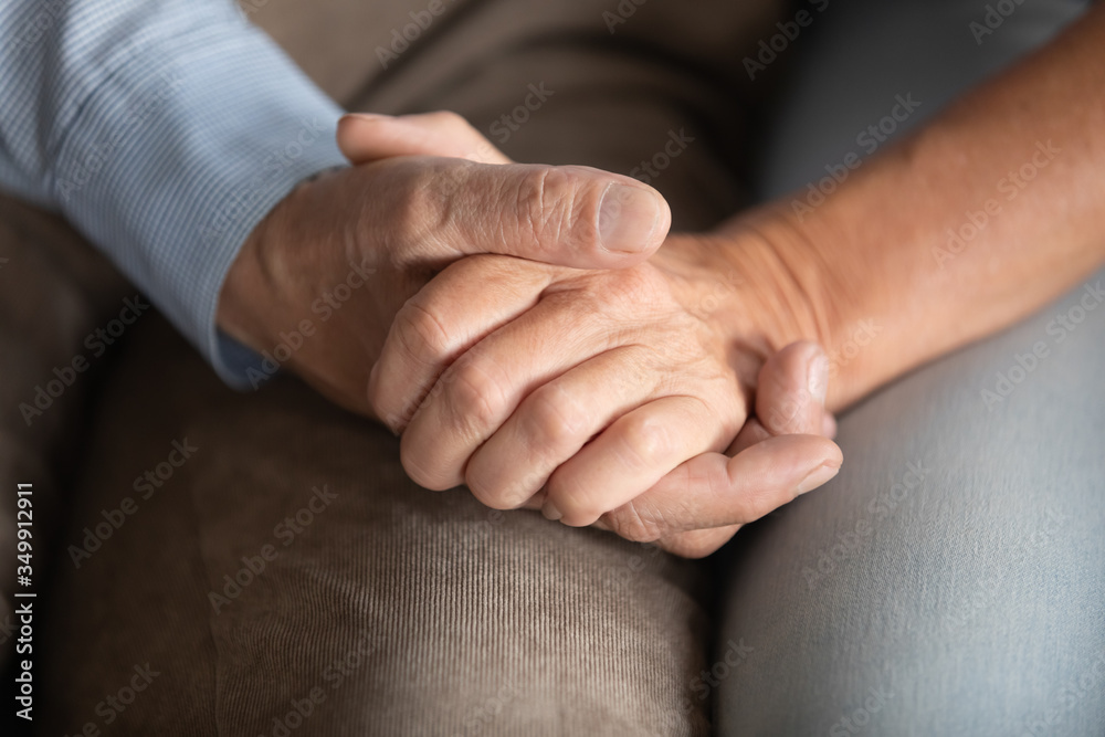 Fototapeta premium Close up senior old man holding hand of mature woman, giving support or psychological help, sharing health complaints, showing love at home. Elderly married family couple having sincere talk together.