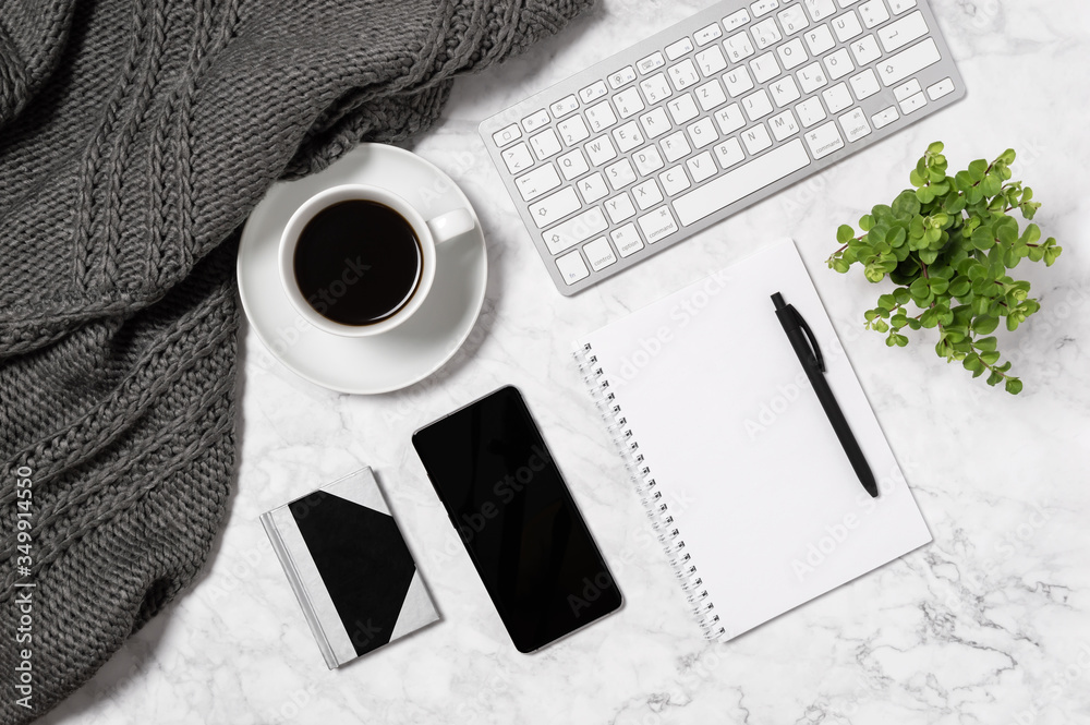 Cozy home office workspace. Marble desk with warm wool plaid, green ivy leaves, coffee cup, keyboard and notebook Cozy home office workspace. Marble desk with warm wool plaid, green ivy leaves, coffee cup, keyboard and notebook