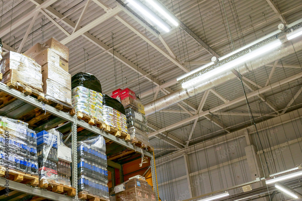 Large rack with products on pallets in a warehouse. Warehouse with products from the bottom up. Many sealed products in a warehouse against a metal ceiling.