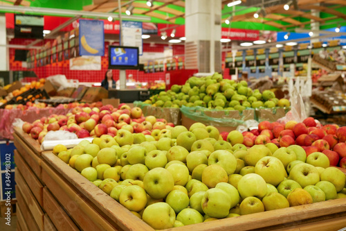 A mountain of green apples lies in a wooden box in a supermarket. A counter of green apples in a store waiting for buyers.