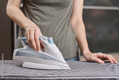 Woman ironing clothes on the ironing board with modern iron