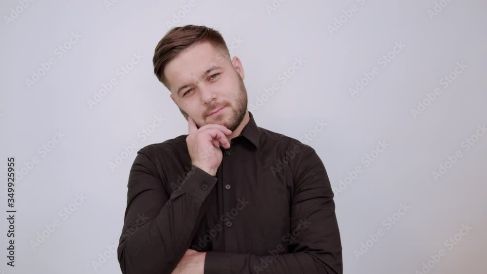 Young Bearded Dark Haired Man In Black Stylish Shirt On White Background, Serious Male Holds Forefinger To His Face And Thinks. The Concept Of Smart People. Young Bearded Dark Haired Man In Black Stylish Shirt On White Background, Serious Male Holds Forefinger To His Face And Thinks. The Concept Of Smart People.