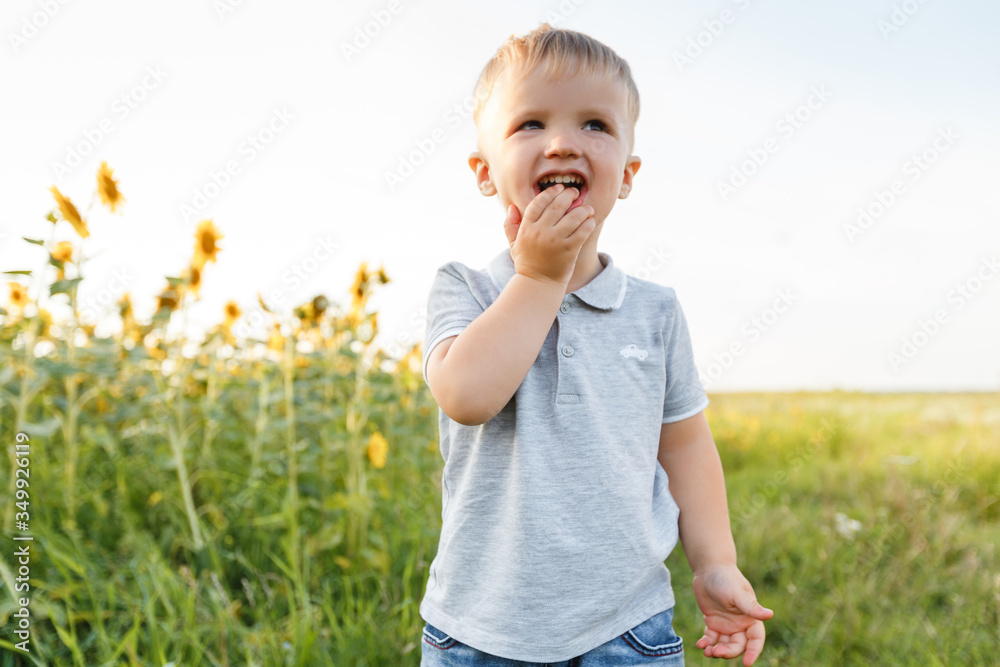 Little boy playing on the background of countryside and smiling. Three years kid having fun in field of sunflowers on sunset. Summer outdoors lifestyle, child leisure, childhood Little boy playing on the background of countryside and smiling. Three years kid having fun in field of sunflowers on sunset. Summer outdoors lifestyle, child leisure, childhood