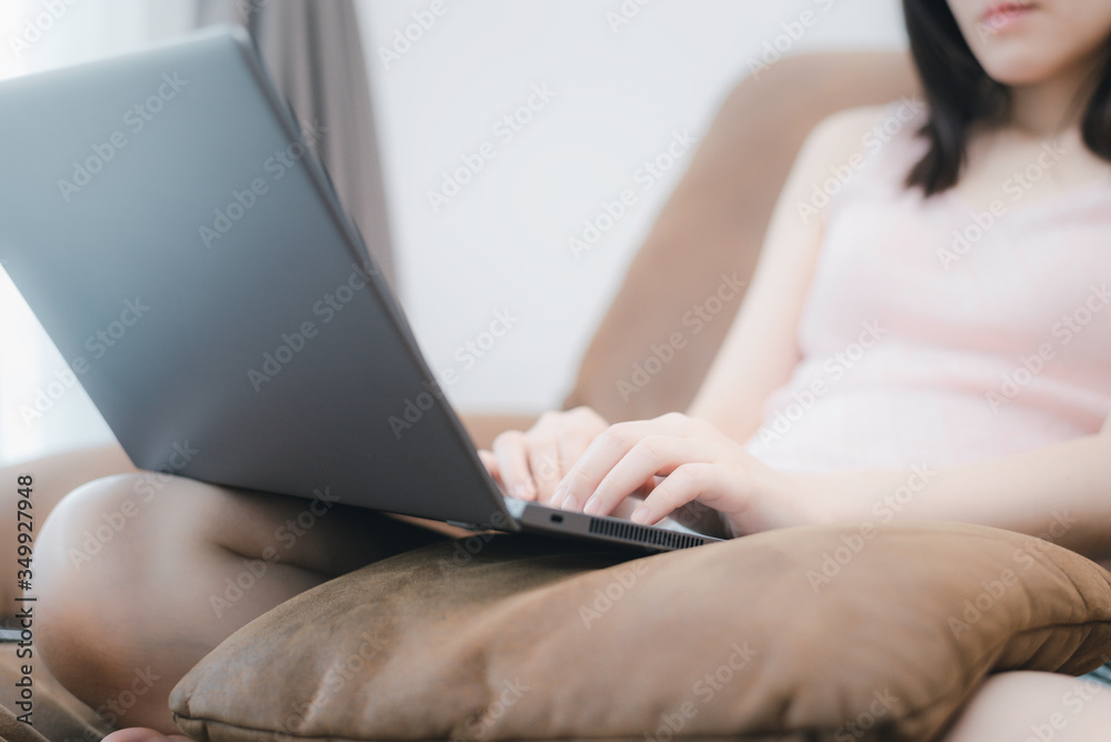 Fototapeta premium Young woman sit on sofa and using laptop computer and use finger typing on key pad. Concept work from home and social distancing from covid-19