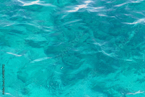 The seabed shines through the light ripples of clear sea water. Azure waves with sun flare.Abstract. Background.