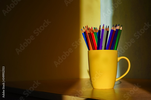 Colored pencils in a yellow mug in the sunlight
