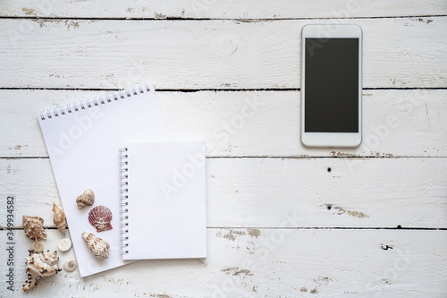 Flat lay phone, notebook with blank and seashell for summer holiday white wood,Top view, copy space