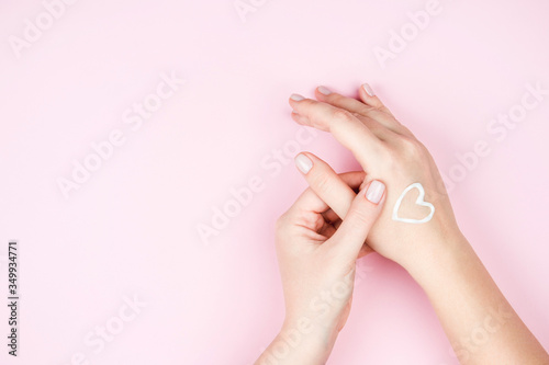Beautiful women s hands with a neat gentle manicure and cream on the skin on a pink background.