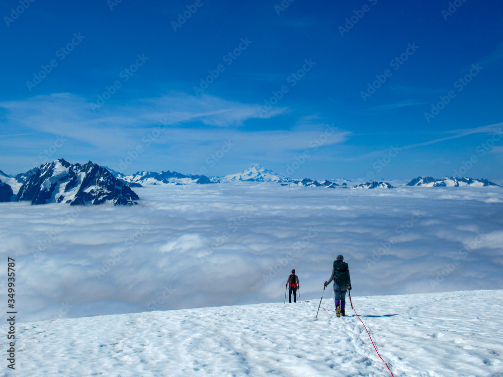 Mountaineers descend mountain glacier above clouds