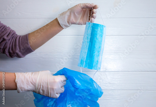 Woman is throwing medical mask away. Utilization of protection during coronavirus. The end of pandemic. Quarantine time finishing. Hands in gloves and blue trash bag. Pollution of environment.