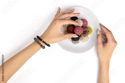 Colorful vegan candies energy balls on a plate with womans hand isolated white background