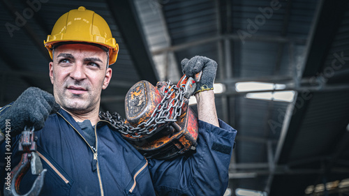 Male industrial worker in blue jumpsuit and hardhat carrying chain hoist on his shoulder. photo